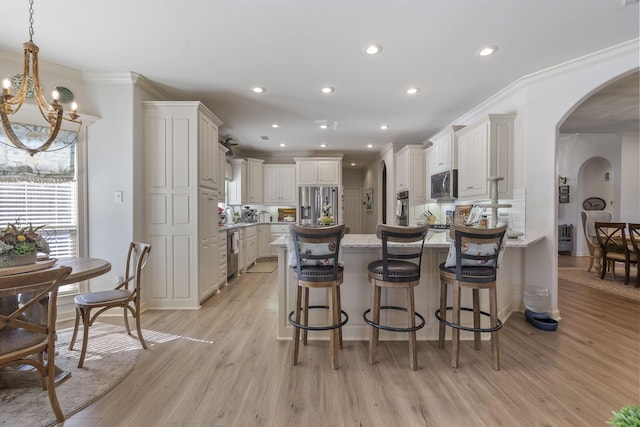 kitchen featuring a breakfast bar, ornamental molding, pendant lighting, stainless steel appliances, and light stone countertops