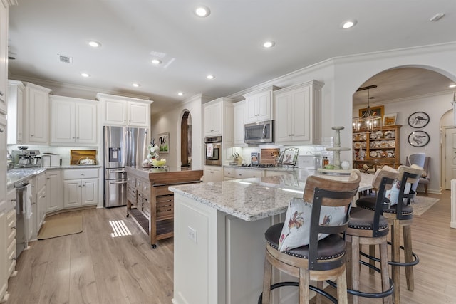 kitchen featuring a kitchen island, appliances with stainless steel finishes, white cabinets, a kitchen breakfast bar, and light stone counters