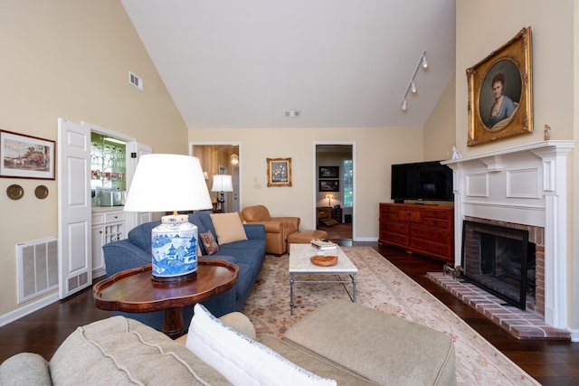 living room with a brick fireplace, dark wood-type flooring, high vaulted ceiling, and rail lighting