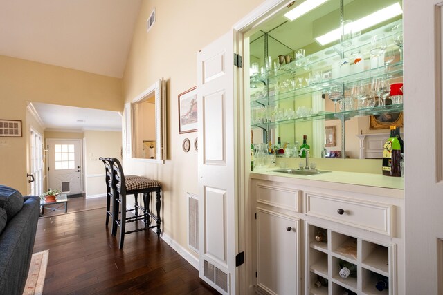 bar featuring dark wood-type flooring, lofted ceiling, crown molding, and sink