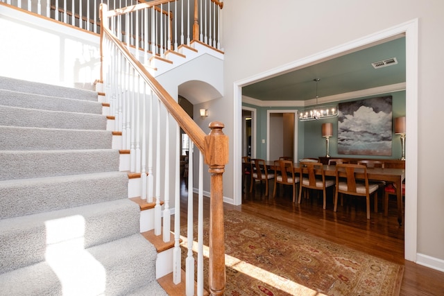 stairs with crown molding, wood-type flooring, a chandelier, and a high ceiling