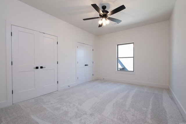 unfurnished bedroom with ceiling fan, light carpet, and two closets