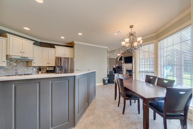 kitchen with tasteful backsplash, stainless steel fridge with ice dispenser, ornamental molding, gray cabinets, and pendant lighting