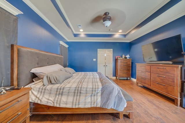 bedroom with a tray ceiling, ornamental molding, ceiling fan, and light wood-type flooring