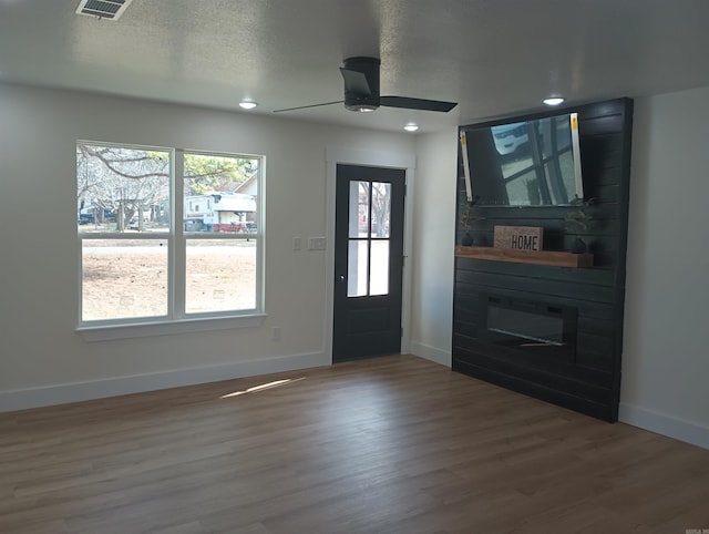 foyer entrance with ceiling fan, wood-type flooring, a fireplace, and a textured ceiling