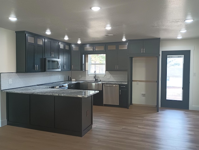 kitchen featuring appliances with stainless steel finishes, hardwood / wood-style floors, stone countertops, decorative backsplash, and kitchen peninsula