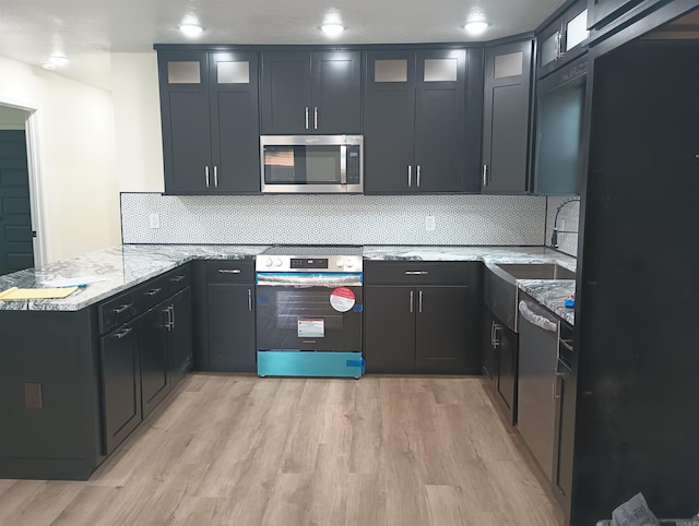 kitchen with kitchen peninsula, sink, light hardwood / wood-style floors, light stone counters, and stainless steel appliances