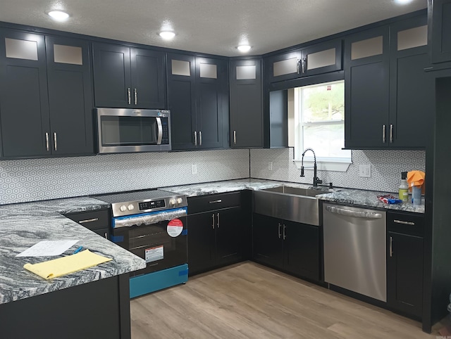 kitchen featuring sink, light stone counters, appliances with stainless steel finishes, light hardwood / wood-style floors, and decorative backsplash