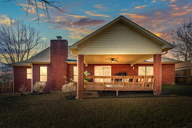 back house at dusk with a wooden deck, ceiling fan, and a lawn