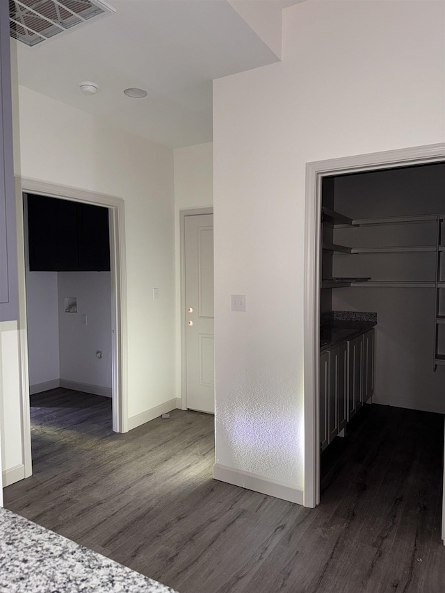 corridor with dark wood-type flooring, visible vents, and baseboards