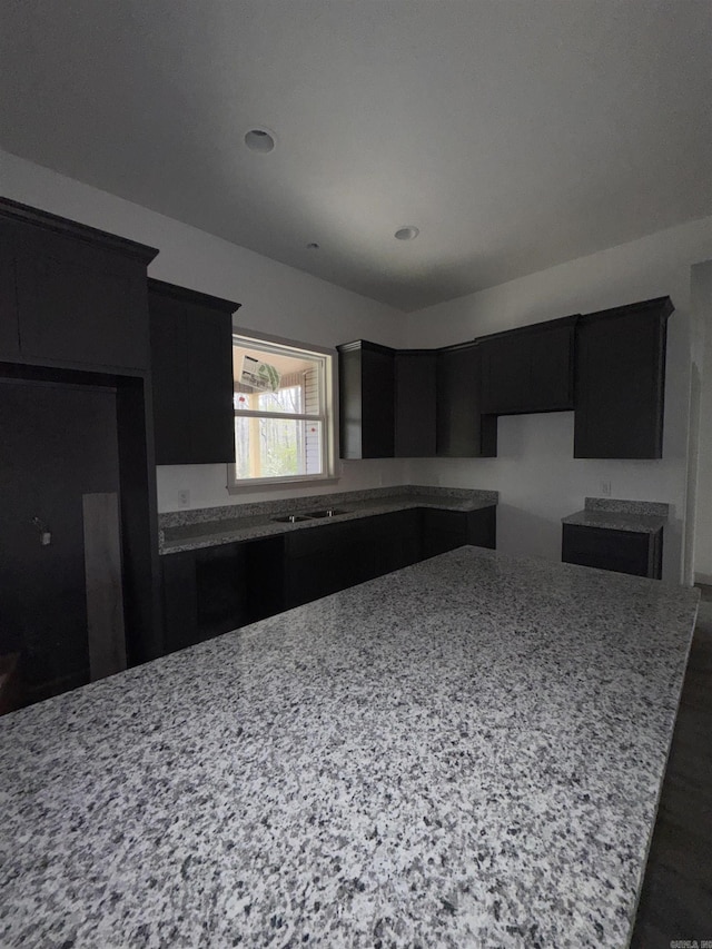 kitchen featuring dark cabinetry, light stone counters, and a sink