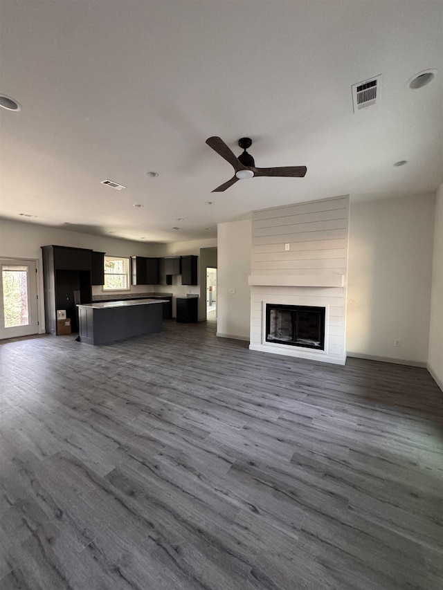 unfurnished living room featuring a wealth of natural light, a large fireplace, visible vents, and dark wood-style flooring