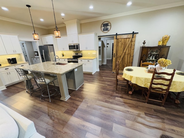 kitchen featuring sink, a center island with sink, stainless steel appliances, a barn door, and white cabinets