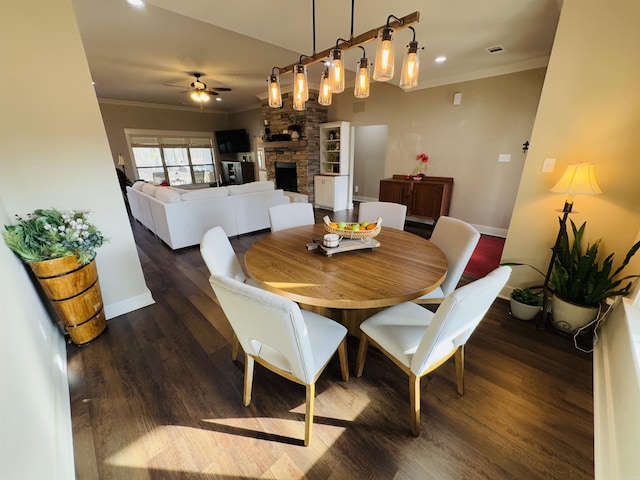 dining room featuring crown molding, ceiling fan, dark hardwood / wood-style flooring, and a stone fireplace