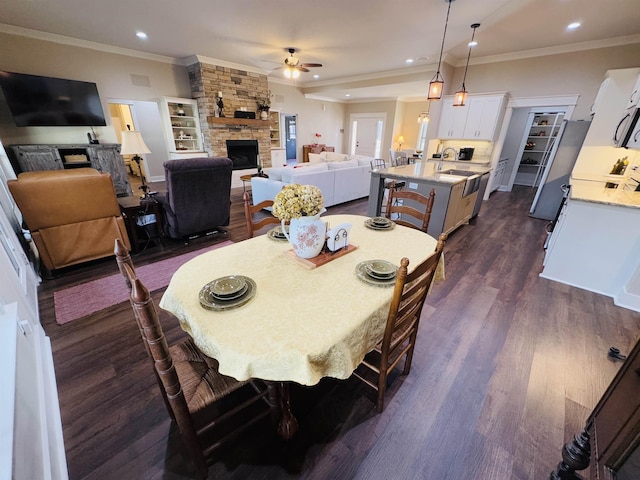 dining room featuring dark wood-type flooring, ceiling fan, ornamental molding, and a stone fireplace