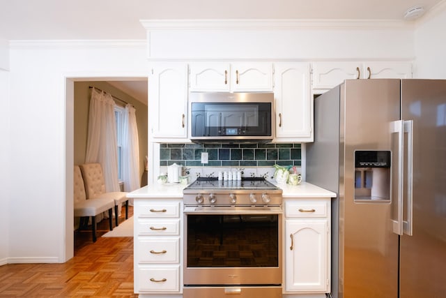 kitchen with light parquet flooring, appliances with stainless steel finishes, ornamental molding, and white cabinets