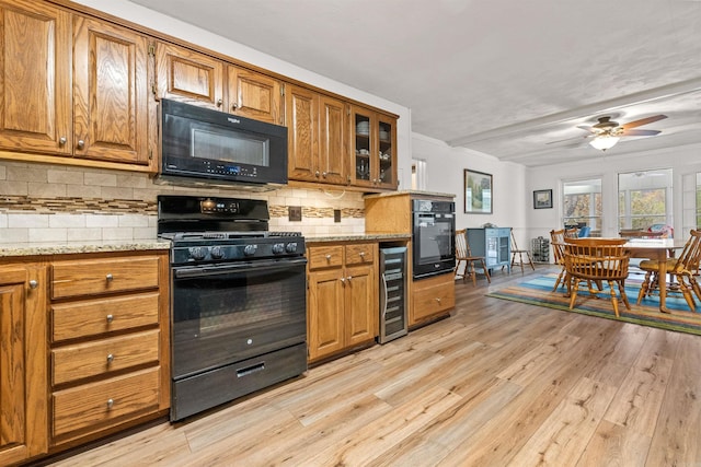 kitchen with wine cooler, tasteful backsplash, light stone countertops, black appliances, and light wood-type flooring