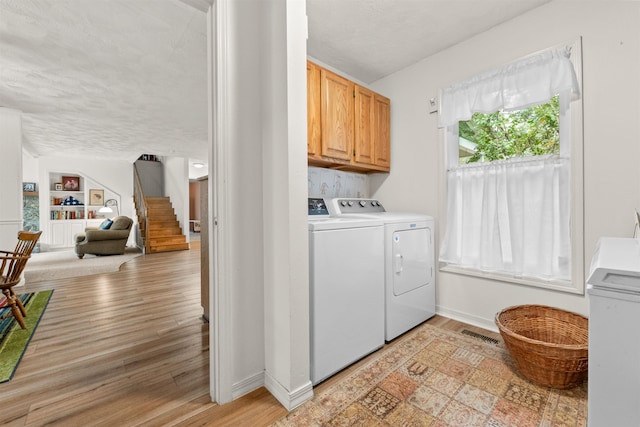 laundry room featuring cabinets, a textured ceiling, washer and dryer, light wood-type flooring, and built in features