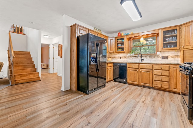 kitchen with sink, backsplash, light stone counters, black appliances, and light wood-type flooring