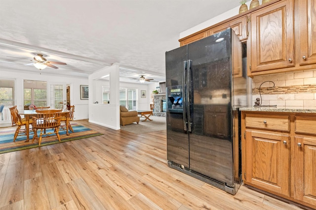 kitchen with a fireplace, tasteful backsplash, ceiling fan, light wood-type flooring, and black refrigerator with ice dispenser