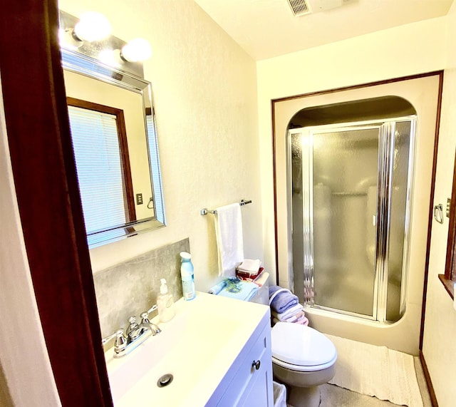 bathroom featuring a shower with door, vanity, and toilet