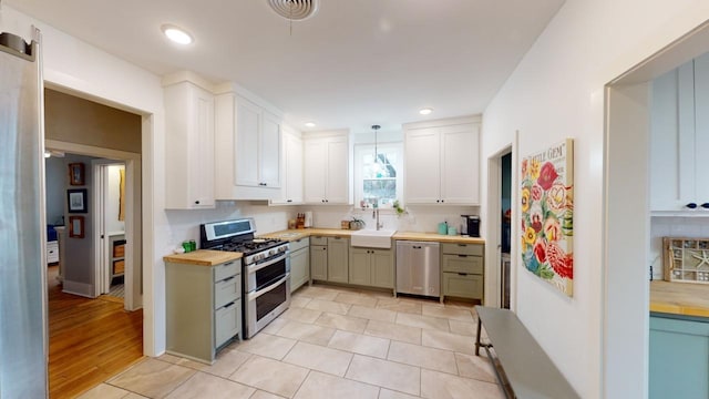 kitchen with butcher block countertops, decorative light fixtures, sink, backsplash, and stainless steel appliances