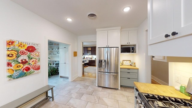 kitchen with stainless steel refrigerator with ice dispenser, gas range oven, light tile patterned floors, and white cabinets