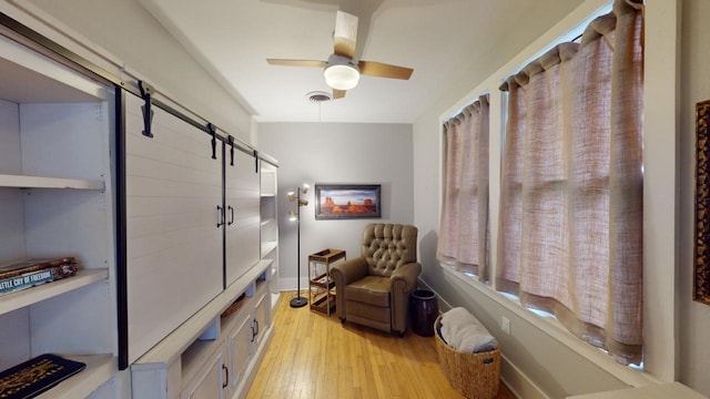 sitting room with a barn door, ceiling fan, and light hardwood / wood-style flooring