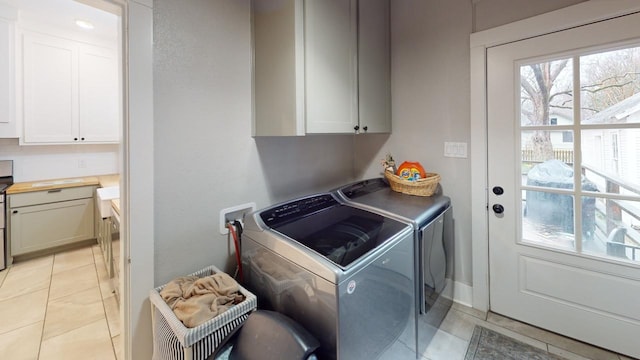 clothes washing area with cabinets, separate washer and dryer, and light tile patterned floors