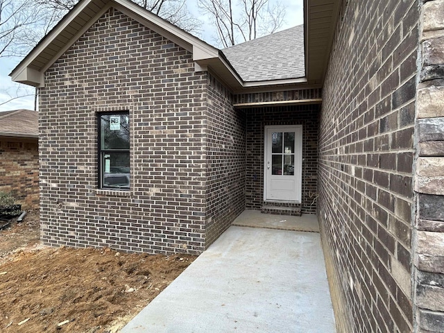 view of exterior entry featuring brick siding and a shingled roof