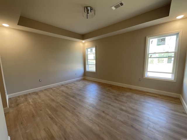 unfurnished room with visible vents, a tray ceiling, wood finished floors, recessed lighting, and baseboards