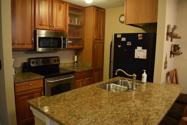 kitchen with appliances with stainless steel finishes, a breakfast bar, sink, light stone counters, and kitchen peninsula