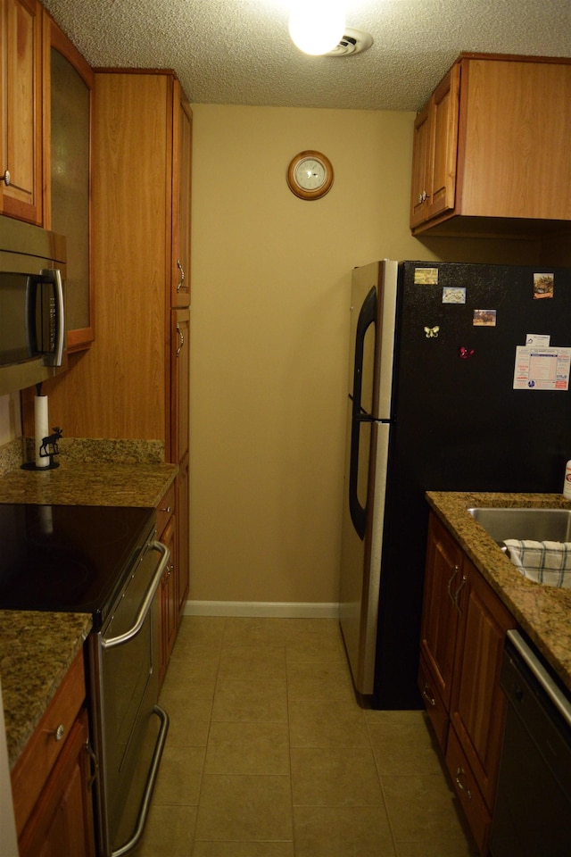 kitchen with sink, a textured ceiling, light tile patterned floors, stone counters, and stainless steel appliances