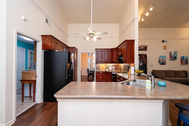 kitchen with sink, black refrigerator, a towering ceiling, a kitchen bar, and kitchen peninsula