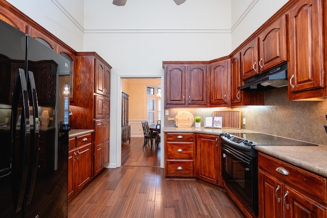 kitchen with backsplash, a towering ceiling, dark hardwood / wood-style floors, and black appliances