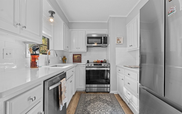 kitchen featuring pendant lighting, sink, white cabinets, hardwood / wood-style flooring, and stainless steel appliances