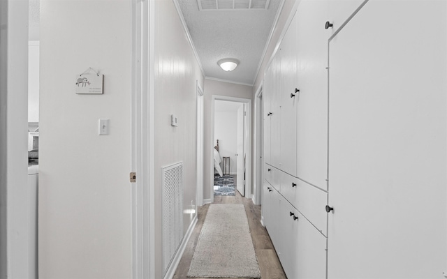 hallway featuring ornamental molding, light hardwood / wood-style flooring, and a textured ceiling