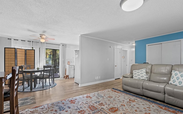 living room with a textured ceiling, light hardwood / wood-style flooring, ornamental molding, and ceiling fan