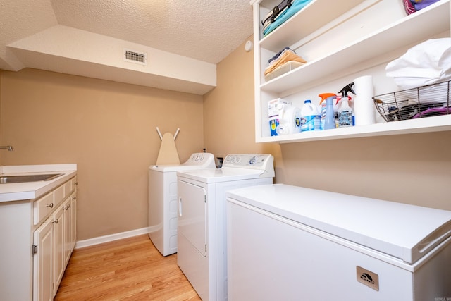 washroom featuring sink, cabinets, washer and dryer, a textured ceiling, and light wood-type flooring