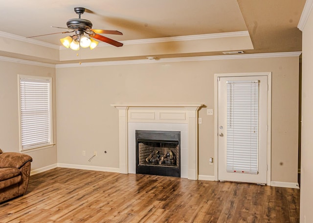 unfurnished living room featuring ceiling fan, ornamental molding, wood-type flooring, and a raised ceiling