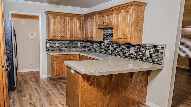 kitchen featuring black refrigerator, sink, light hardwood / wood-style floors, kitchen peninsula, and crown molding