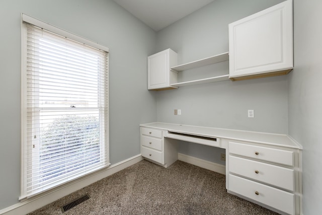 unfurnished office featuring plenty of natural light, built in desk, and carpet