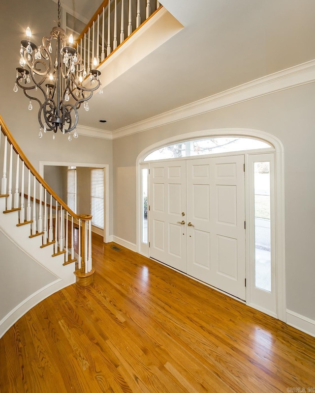 foyer entrance with crown molding, wood-type flooring, and an inviting chandelier