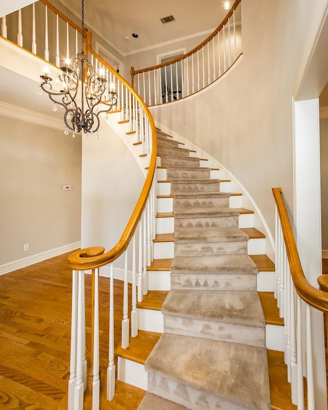 stairs featuring wood-type flooring, a towering ceiling, an inviting chandelier, and crown molding