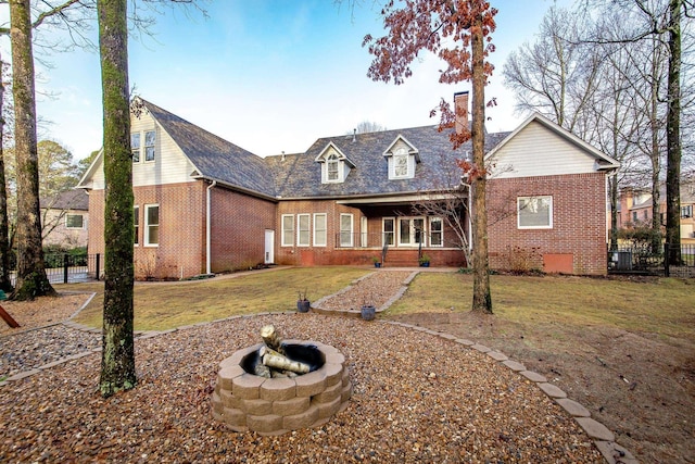 back of house with an outdoor fire pit and a lawn