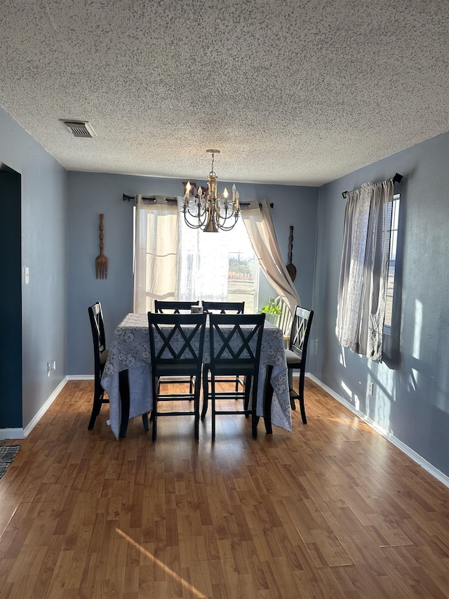 dining space with dark hardwood / wood-style floors, a textured ceiling, and an inviting chandelier