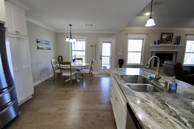 kitchen featuring sink, stainless steel refrigerator, hanging light fixtures, light stone counters, and white cabinets