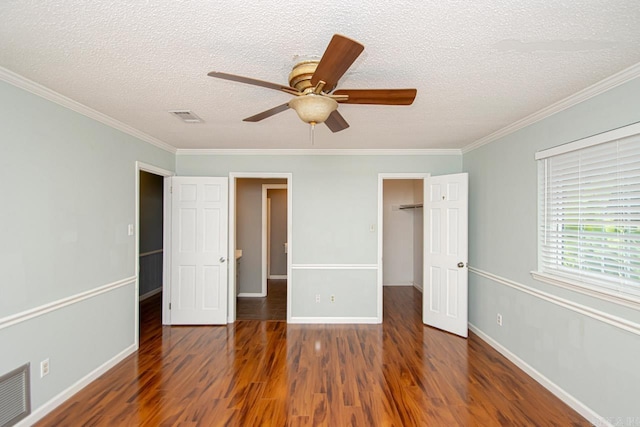 unfurnished bedroom with dark wood-type flooring, a walk in closet, a textured ceiling, ornamental molding, and a closet