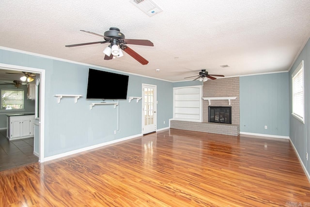 unfurnished living room featuring a fireplace, hardwood / wood-style flooring, ornamental molding, ceiling fan, and a textured ceiling