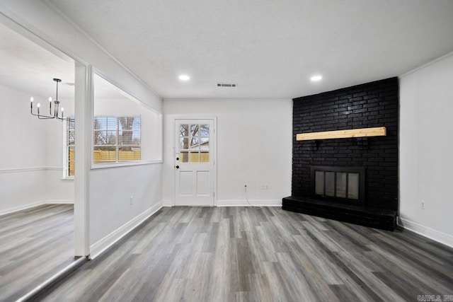 unfurnished living room featuring hardwood / wood-style flooring, crown molding, a brick fireplace, a textured ceiling, and an inviting chandelier